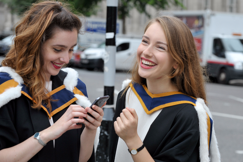 Two graduates laughing outside the RCM on graduation day